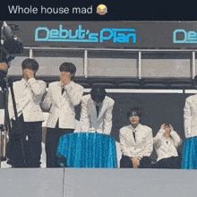 a group of men sitting in front of a debut 's plan sign