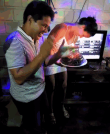 a man and woman are celebrating a birthday with a cake in front of a computer monitor