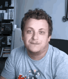 a man with curly hair is wearing a grey t-shirt and making a funny face .