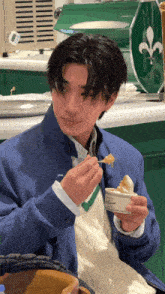 a man in a blue jacket is eating a piece of food with a spoon