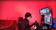 a man wearing headphones sits in front of a computer monitor with a red background