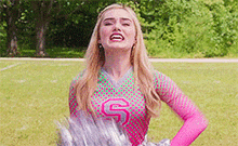 a cheerleader is holding a bunch of pom poms on a field and smiling .