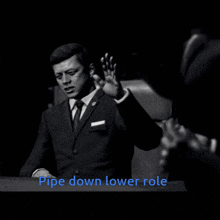 a black and white photo of a man in a suit and tie with the words pipe down lower role above him