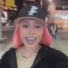 a woman with pink hair is wearing a black hat with a white letter x on it