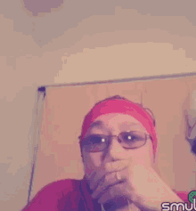 a woman wearing glasses and a headband is covering her mouth with her hand