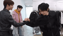 three young men shake hands in a room with clothes hanging on the wall