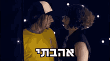 a man in a yellow shirt is kissing a woman in a black hat with hebrew writing on the bottom