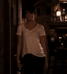 a woman in a white shirt and black pants is standing in a dark room