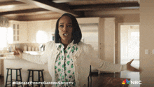 a woman is standing in a kitchen with her arms outstretched and the words grosse pointe garden society on the bottom right