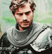a man with a beard and a scarf around his neck is wearing a knight 's armor .