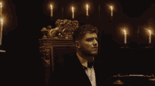 a man in a tuxedo is sitting in a chair with candles in the background