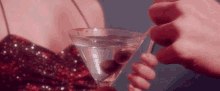 a woman in a sequined dress is holding a martini with olives in it .