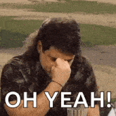 a man with a mullet is covering his nose with his hand while sitting at a table .