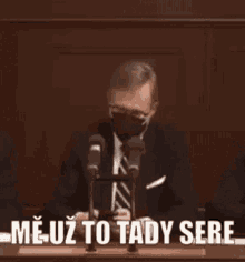 a man in a suit and tie is speaking into a microphone while wearing a face mask .