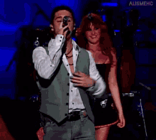 a man in a green vest is singing into a microphone on stage