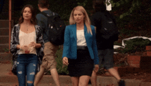 a woman in a blue jacket and a woman in a black skirt walk down a sidewalk