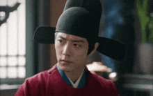 a man in a red shirt and a black hat is looking at the camera .