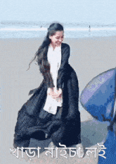 a woman in a black dress is dancing on a beach with a blue surfboard in the background