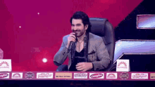 a man is singing into a microphone while sitting at a table with advertisements on it