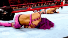 a woman is laying on the ground in a wrestling ring while another woman is standing in the ring .