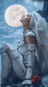 a woman with long white hair is sitting on a rock with a rose in front of a full moon .