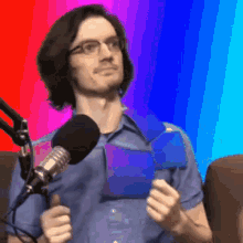 a man wearing glasses is standing in front of a microphone holding a blue item .