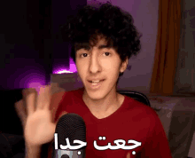 a young man in a red shirt is waving in front of a blue yeti