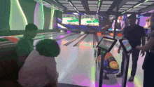 a group of people are playing a game of bowling at a bowling alley with a basketball game on the screens