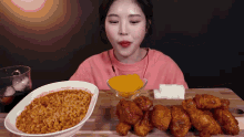 a woman in a pink shirt is eating a bowl of ramen and fried chicken