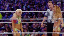 two female wrestlers are standing in a wrestling ring with a referee .