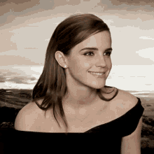 a woman wearing a black off the shoulder top smiles for the camera