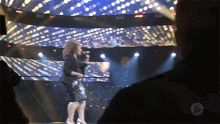 a woman singing into a microphone on a stage in front of a large screen