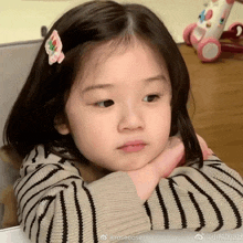 a little girl wearing a striped sweater and a pink hair clip