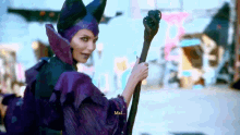 a woman in a purple costume is holding a cane and says mal