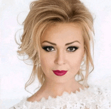 a woman wearing a white lace top and pink lipstick looks at the camera