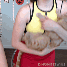 a woman in a yellow tank top is holding a cat in her arms and the words dinomitetwins are on the bottom