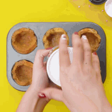 a person is pouring a cup of ice cream into a muffin pan .
