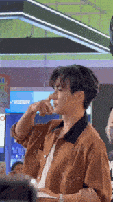 a man in a brown shirt is touching his nose while standing in front of a vending machine that says vesper