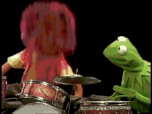 kermit the frog playing drums next to a girl