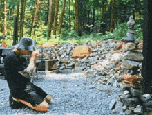 a man wearing a hat is kneeling down in front of a pile of rocks
