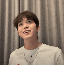 a young man wearing a white shirt and a necklace with a heart on it