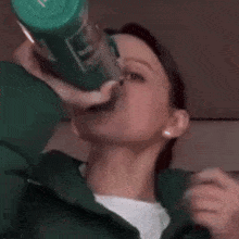 a woman in a green jacket is drinking from a green cup