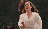 a woman in a white lace top sings into her mouth