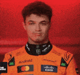 a young man wearing an orange racing suit with logos for android and cisco