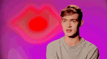 a young man is standing in front of a pink background with a red heart behind him .