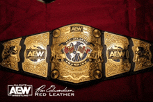 a gold and black aew belt with a red leather logo