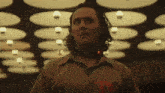 a man with long hair and a collar around his neck is standing in front of a ceiling .