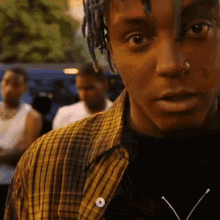 a man with dreadlocks and a nose ring is wearing a plaid shirt .