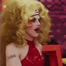 a drag queen is wearing a red dress and a wig .