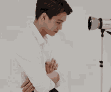 a young man in a white shirt is standing with his arms crossed in front of a camera .